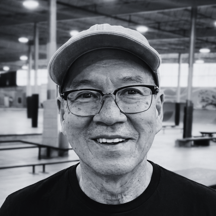 Headshot of Dr. Jack Schmit, Board President at The Warehouse, smiling warmly while wearing glasses and a baseball cap inside an indoor skatepark facility.
