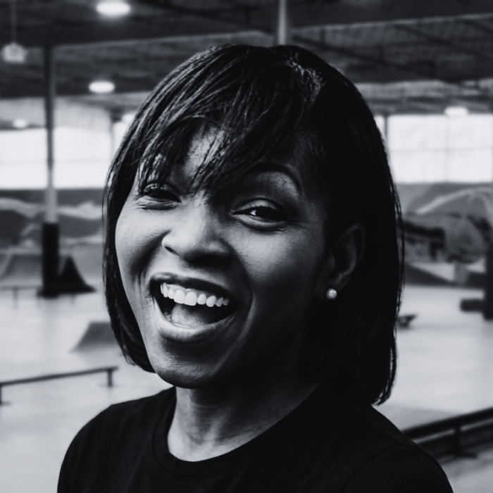 Headshot of Dr. Tracey Warren, Board Member at The Warehouse, smiling with shoulder-length blonde hair and a dark shirt inside an indoor skatepark facility.