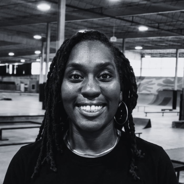 Headshot of Candace, Floor Staff and Kids Programming lead at The Warehouse, smiling brightly with long dreadlocks and hoop earrings inside an indoor skatepark facility.