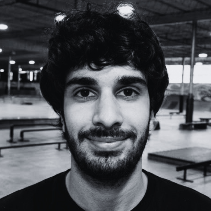 Headshot of Henrique, Floor Staff member at The Warehouse, smiling with thick wavy dark hair, a mustache, and a short beard inside an indoor skatepark facility.