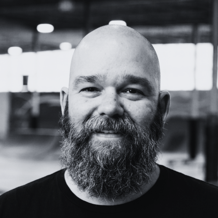 Headshot of Josh, Administrative Assistant at The Warehouse, smiling with a full beard and shaved head inside an indoor skatepark facility