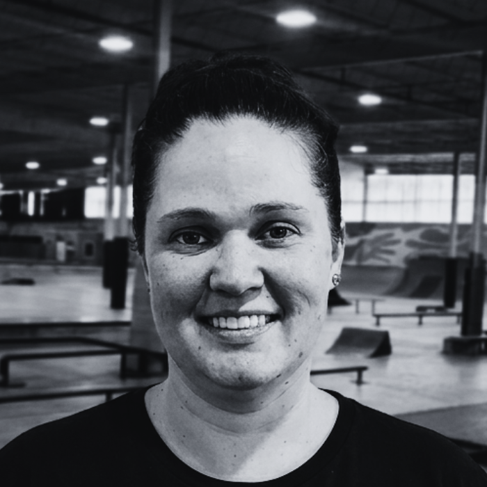 Headshot of Margo, Snack Coordinator and Floor Staff member at The Warehouse, smiling with her hair tied back in a bun inside an indoor skatepark facility.