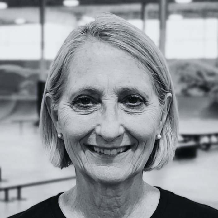 Headshot of Nancy Weil, Floor Staff member at The Warehouse, smiling brightly with styled shoulder-length dark hair and glasses inside an indoor skatepark facility.